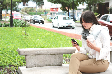 Young latin woman with her mobile phone and cup of coffee