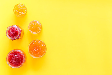 Set of sweet jams in glass jars on yellow background top view copy space