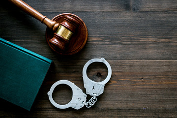 Crime concept. Metal handcuffs near judge gavel and law book on dark wooden background top view copy space