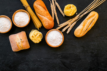Bakery production, making bread and pasta. Fresh bread and raw pasta near flour in bowl and wheat ears on black background top view copy space