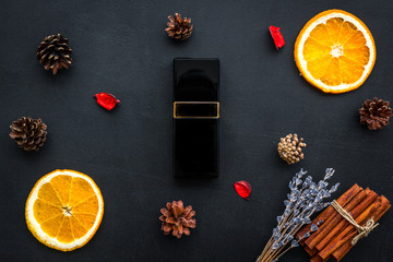 Fruity and pine perfume for women. Bottle of perfume near orange, lavender, cinnamon, pine cones on black background top view pattern