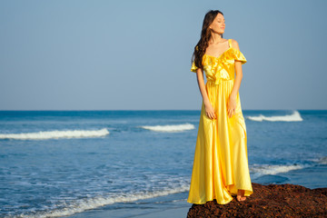 Fototapeta na wymiar Beautiful woman wearing yellow silk flowing dress walking on beach