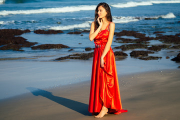 Beautiful woman with flying long butterfly sexy res dress posing on beach against the backdrop of tropical trees and palm trees