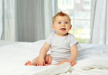 Charming blue-eyed baby 10 months in bed in a striped jumpsuit