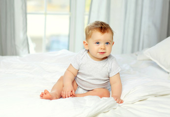 Charming blue-eyed baby 10 months in bed in a striped jumpsuit