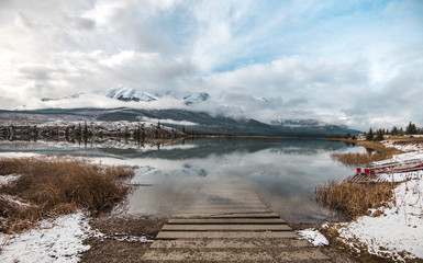 A boat launch slides its way into the calm alpine lake water below snow covered peaks on an overcast winter day