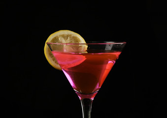 piece of lemon is thrown into a glass with pink cocktail on a dark background