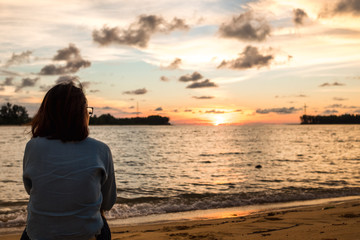 travel concept women sitting alone on beach with sunset and sea background