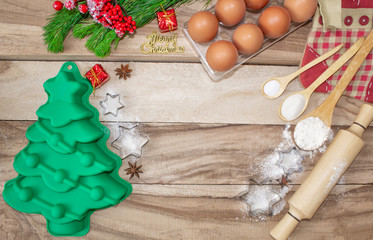 Fototapeta na wymiar Christmas baking cake background. Ingredients and tools for baking - flour, eggs, silicone molds in the shape of a Christmas tree, and a rolling pin on a wooden background. With free text space.