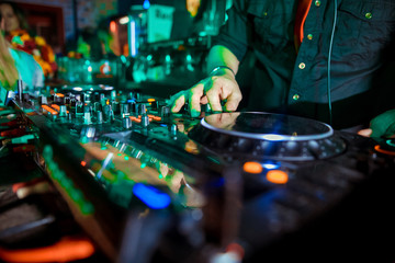 Dj mixes the track in the nightclub at party. Headphones in foreground and DJ hands in motion