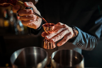Closeup shot of bartender hand stirring a negroni cocktail. Glass of drink on counter with...