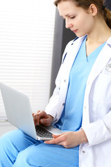 Woman doctor typing on laptop computer while working in hospital office. Data in medicine and health care