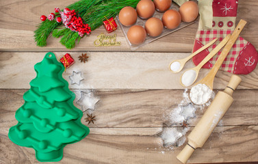 Fototapeta na wymiar Christmas baking cake background. Ingredients and tools for baking - flour, eggs, silicone molds in the shape of a Christmas tree, and a rolling pin on a wooden background. With free text space.