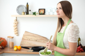Young woman cooking in the kitchen. Housewife slicing fresh salad