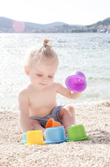 Cute baby playing with plastic toys on the pebble beach near the sea