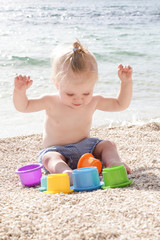 Cute baby playing with plastic toys on the pebble beach near the sea
