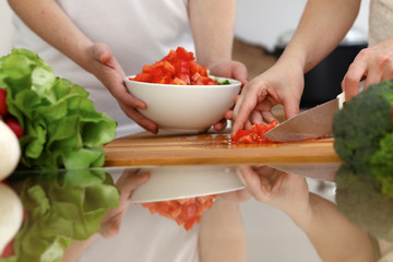 Closeup of human hands cooking in kitchen. Mother and daughter or two female friends cutting vegetables for fresh salad. Friendship, family dinner and lifestyle concepts