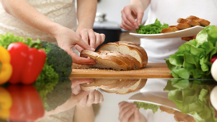 Closeup of human hands cooking in kitchen. Mother and daughter or two female friends cutting bread for dinner. Friendship, family and lifestyle concepts