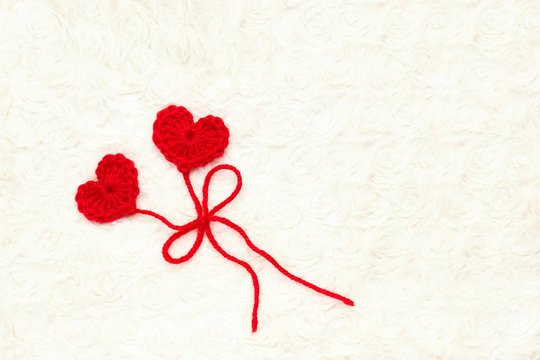 Two red crochet wool hearts and ribbon on white crochet background. The concept for 14 February, romantic Valentine day, love affair, love story. Festive overhead photo with place for text, copyspace.