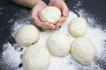 Kid's hands, some flour an wheat dough on the black table. Children hands making the rye dough for backing bread or pizza. Small hands with dough. Little child preparing dough for backing pie.