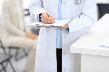 Doctor woman filling up medical form while standing near reception desk at clinic or emergency hospital.Unknown physician at work, hands close-up. Medicine and patient service concept