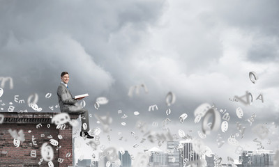 Man on roof edge reading book and symbols flying around