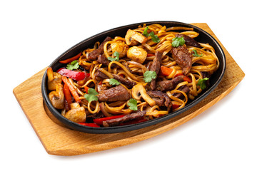 Traditional chinese food - pan of udon noodles with beef and vegetables at wooden board isolated at white background.