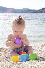Cute baby playing with plastic toys on the pebble beach near the sea