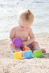 Cute baby playing with plastic toys on the pebble beach near the sea