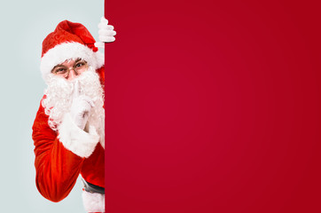 Santa Claus with finger on lips asking for silence with colorful advertisement board and copy space