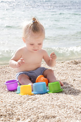 Cute baby playing with plastic toys on the pebble beach near the sea