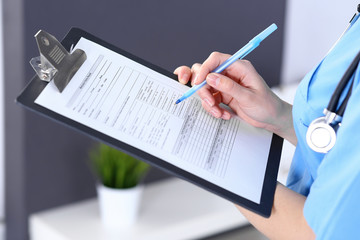 Female doctor filling up medical form on a clipboard, closeup. Healthcare, insurance and medicine concept