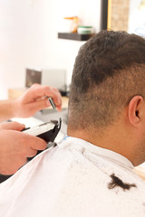Fototapeta premium Back view of man getting short hair trimming at barber shop with clipper machine