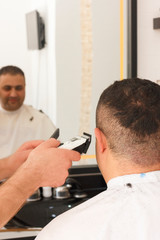 Fototapeta premium Back view of man getting short hair trimming at barber shop with clipper machine