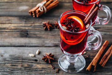 Mulled red wine with spices and orange in glass on a wooden rustic background.