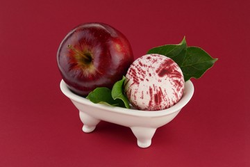 Bath Bomb with apple extract. Striped bath bomb and a red apple in a decorative bath on a  burgundy...