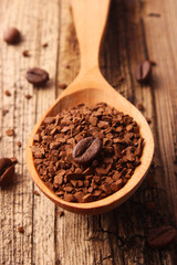 instant coffee in a wooden spoon and coffee beans on a wooden background.
