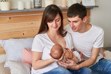 young parents with a newborn baby at home on the bed