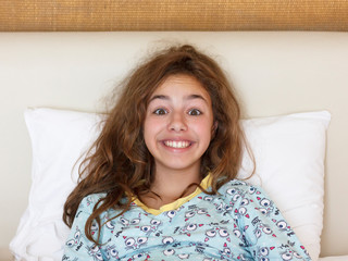 Naklejka premium Just awake pretty teenager girl with funny emotion face and wild hair on the bed