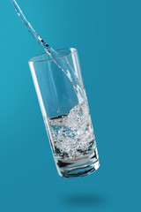 water is poured into a tall glass, the glass flies over the blue surface, water bubbles