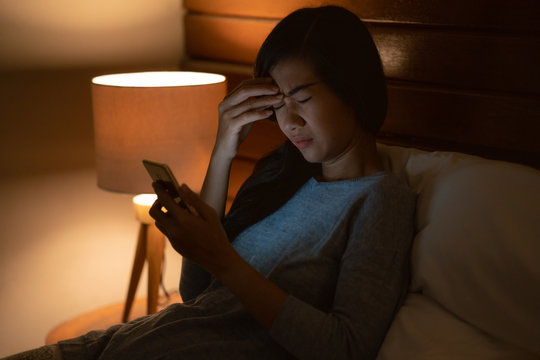 stress asian woman lying in bed using smartphone