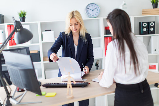 Two girls stand in the office bent over near the table and work with documents.