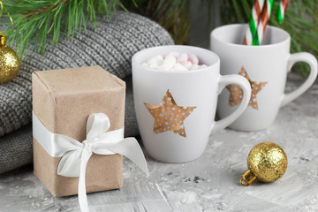 gift box and cute cups with marshmallows and candy canes under christmas tree