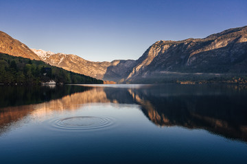 Sunrise view of alpine lake Bohinj with blue sky, sunlight and mist over water. Circles in water. Famous lake of Bohinj in Triglav National Park, Julian alps, Slovenia.