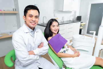 Obraz premium young girl patient sitting on dental chair and talking to male dentist stomatologist while he taking necessary notes in medical record