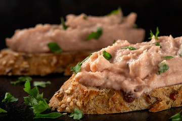 Two slices of bread with vegetable pate and chopped green parsley on a dark slate