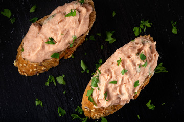 Two slices of bread with vegetable pate and chopped green parsley on a dark slate
