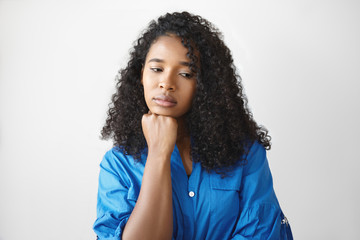 Fototapeta na wymiar Upset beautiful young Afro American female in blue shirt looking down resting chin on her hand, feeling sad and lonely on her birthday. Negative human emotions, sadness and loneliness concept