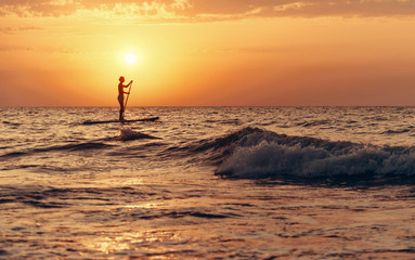 Silhouette of man on paddle board in sea at sunset.