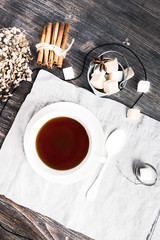 Cup of black tea on wooden table with cane and white sugar cubes, tea spoon and tea strainer. Top view. Bleached by design. 